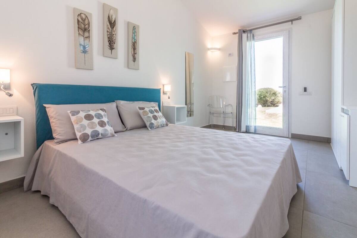 Een slaapkamer met een groot bed, een blauwgroen hoofdeinde en een schuifdeur naar een balkon.