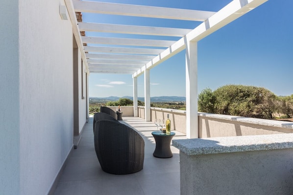 Un espacio exterior techado con una pérgola, asientos y vistas al paisaje.