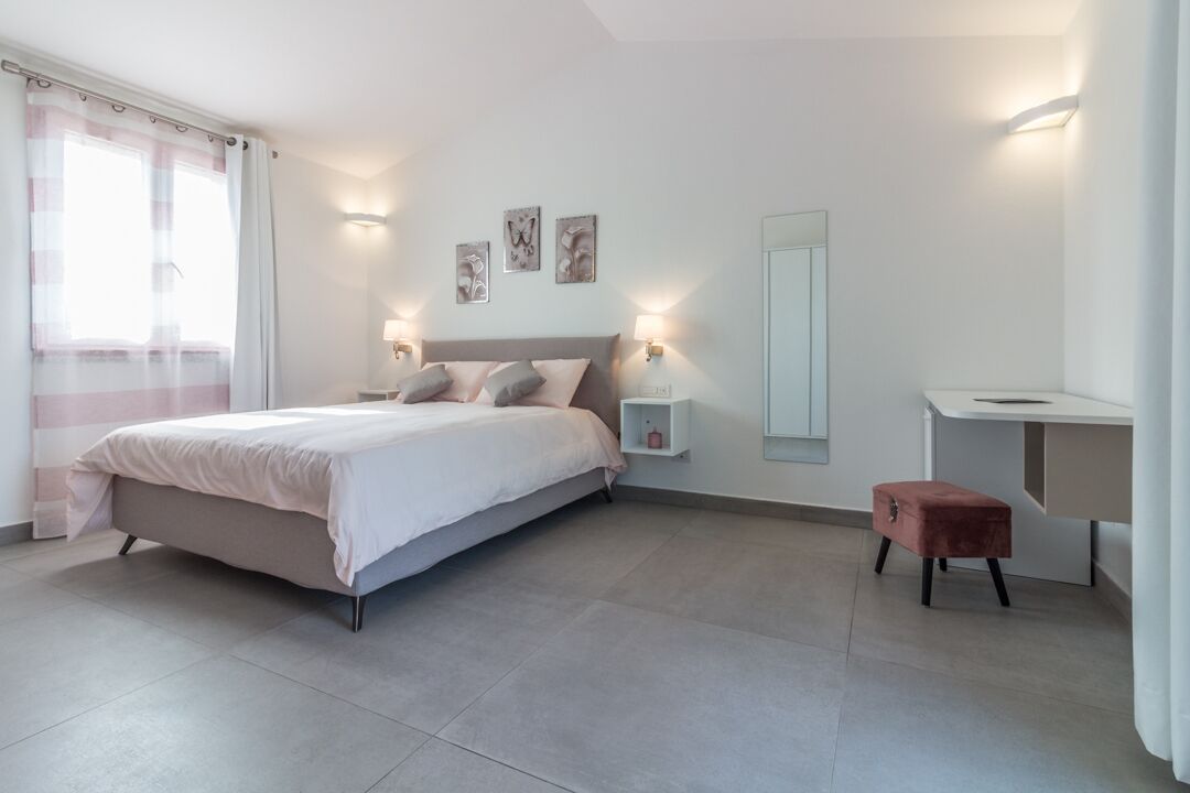 A modern bedroom with a large bed, bedside lamps, a small bedside table, a mirror, and a desk.