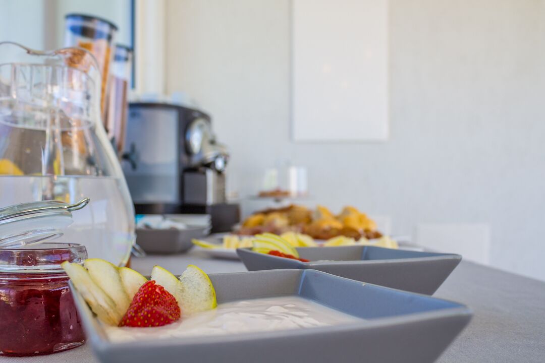 A breakfast setting with a pitcher, a jar of jam, and a plate with sliced fruit and yogurt.