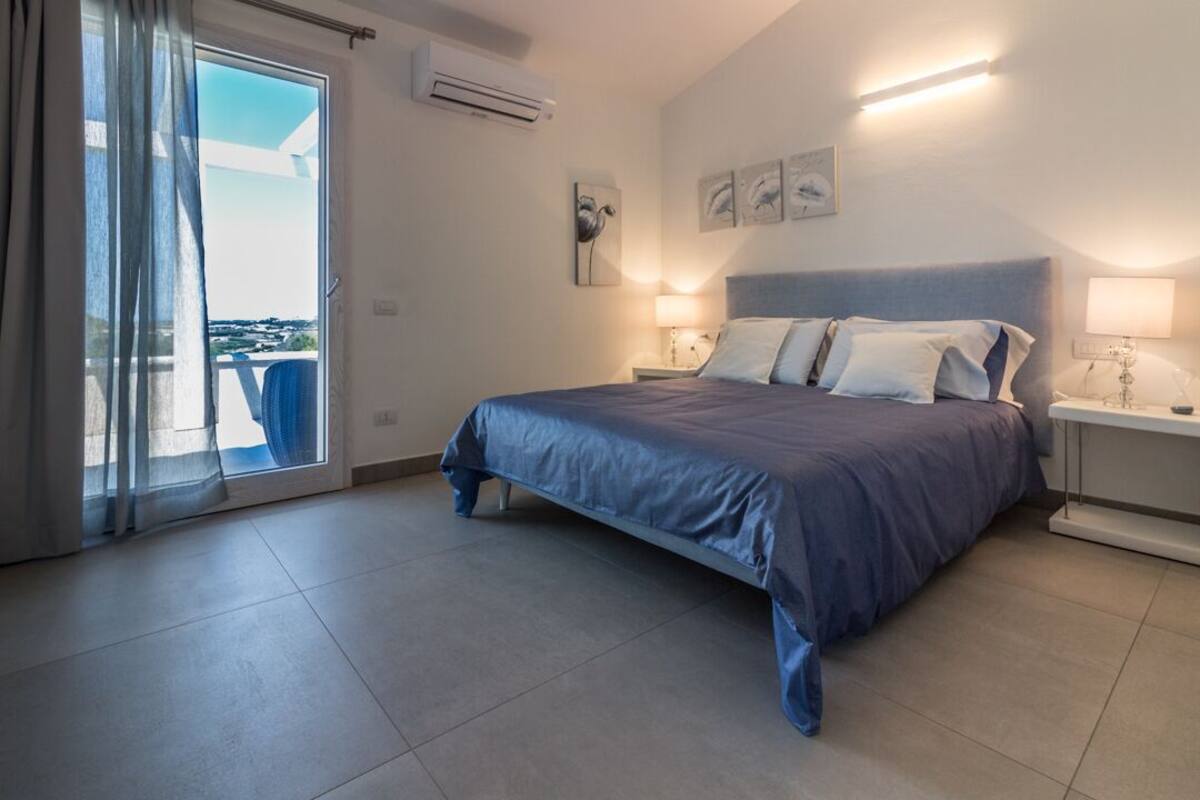 Een slaapkamer met een bed, twee nachtkastjes, een raam met gordijnen en uitzicht op de omgeving.