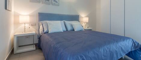 A bedroom with a large bed, two bedside tables with lamps, and a wardrobe.