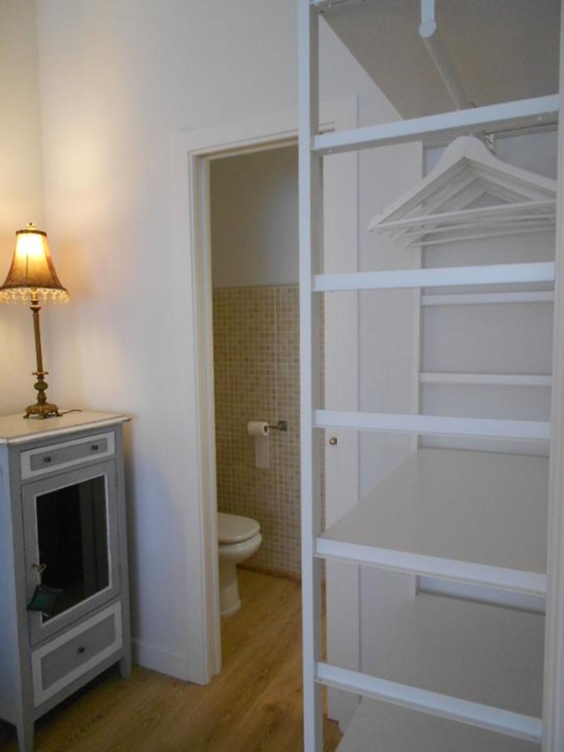 A bathroom with a toilet, a small cabinet, and a lamp.