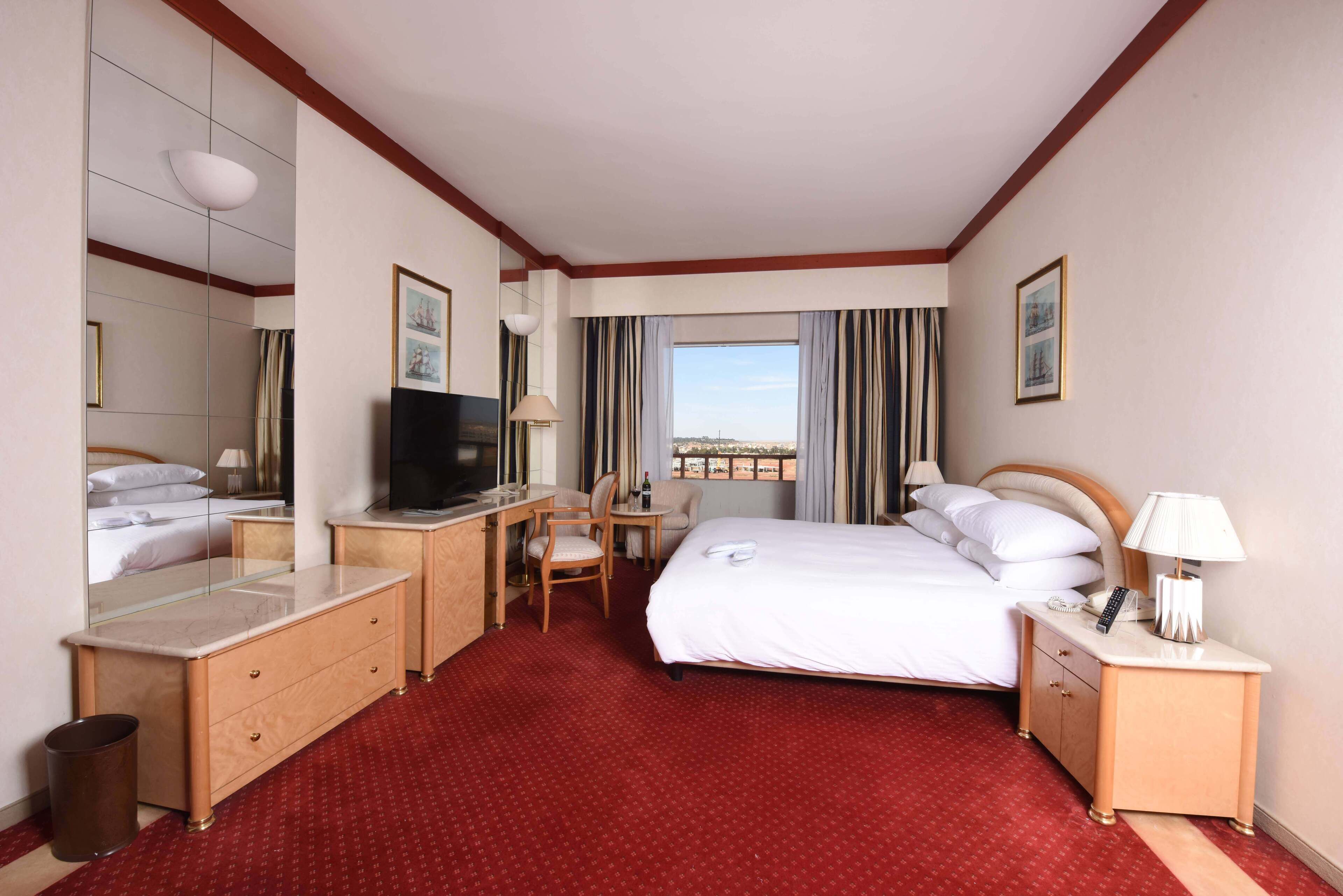 Habitación de hotel con cama, escritorio, silla, televisión, lámpara y vistas de la ciudad.