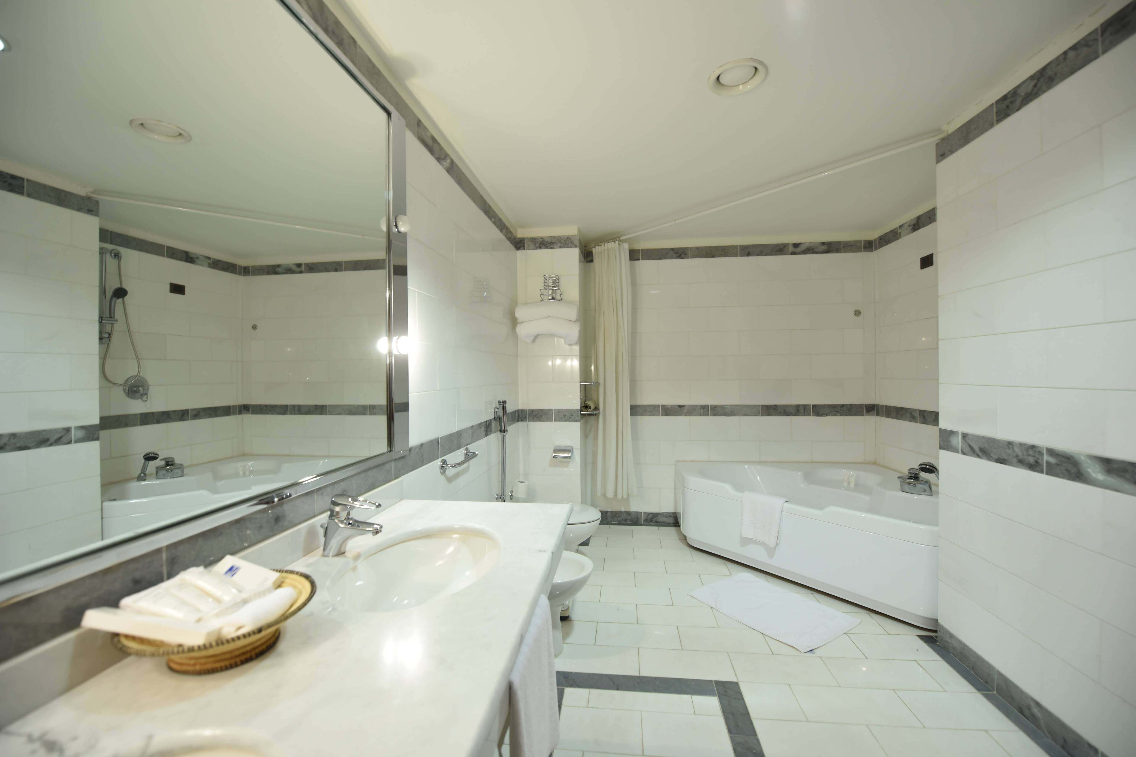 A modern bathroom with a large mirror, a sink, a toilet, and a bathtub.