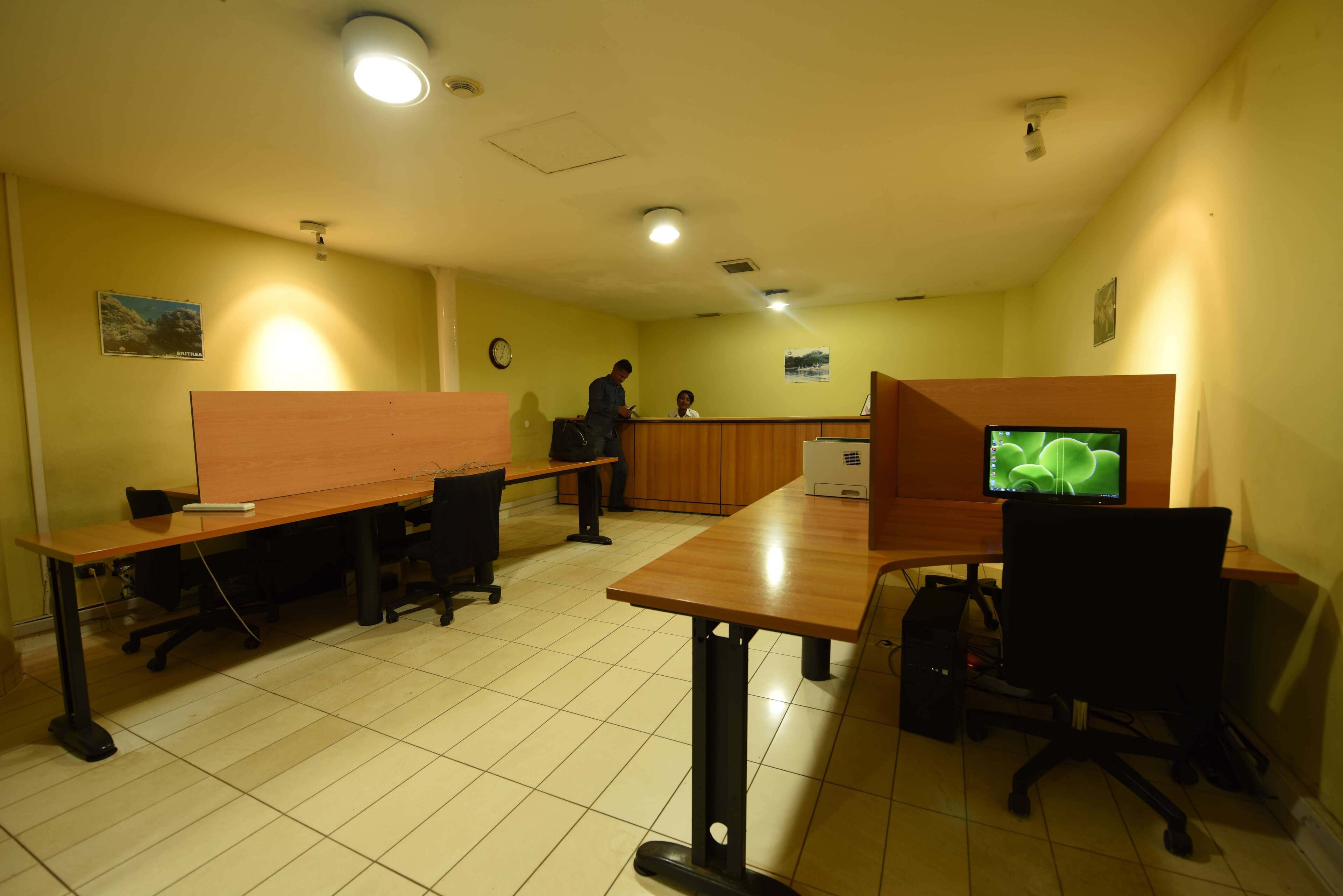 A conference room with long tables, chairs, a wooden partition, a clock, and a computer monitor.
