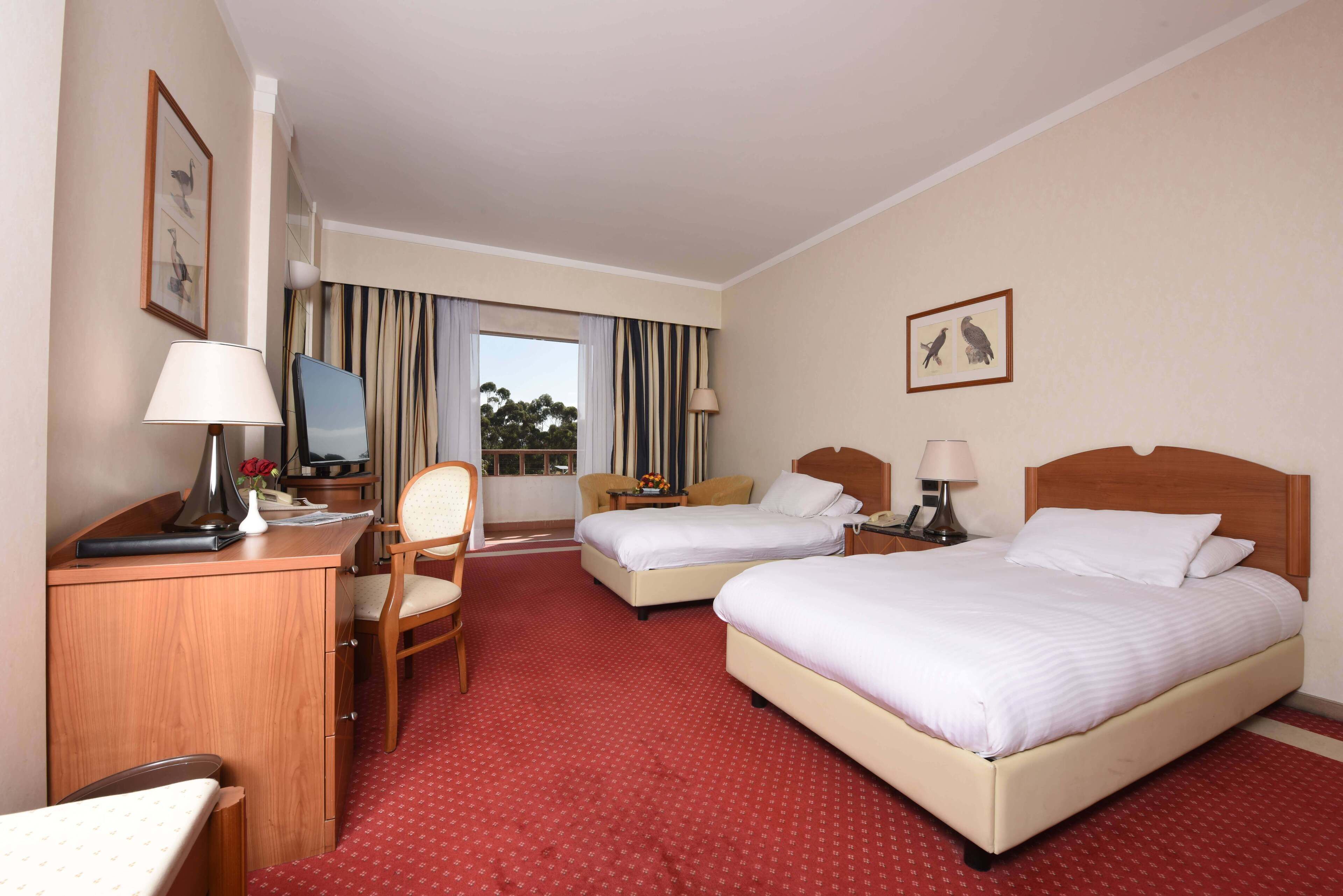 A hotel room with two beds, a desk, a chair, and a TV.