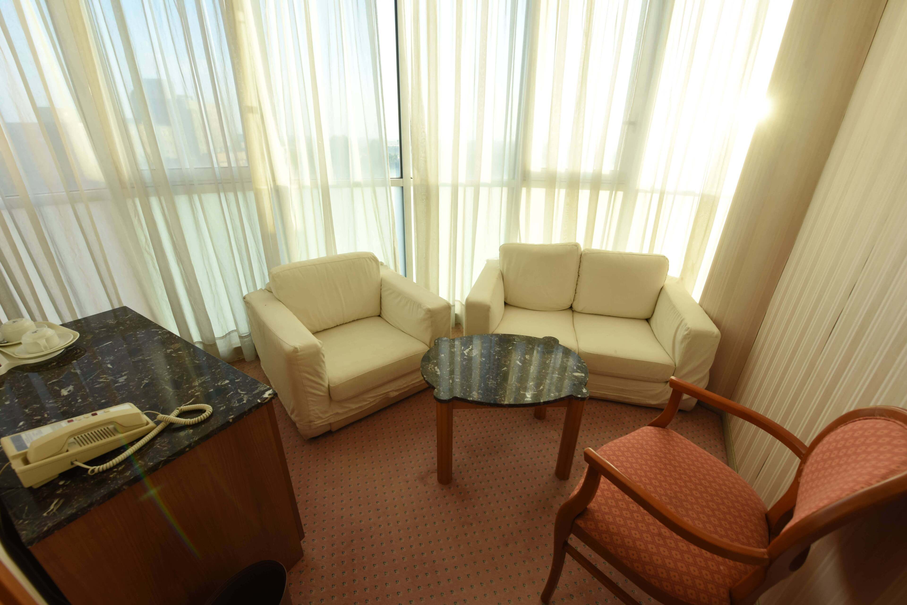 Hotellihuone, jossa on sohvaryhmä, pieni pöytä ja puhelin työpöydällä.