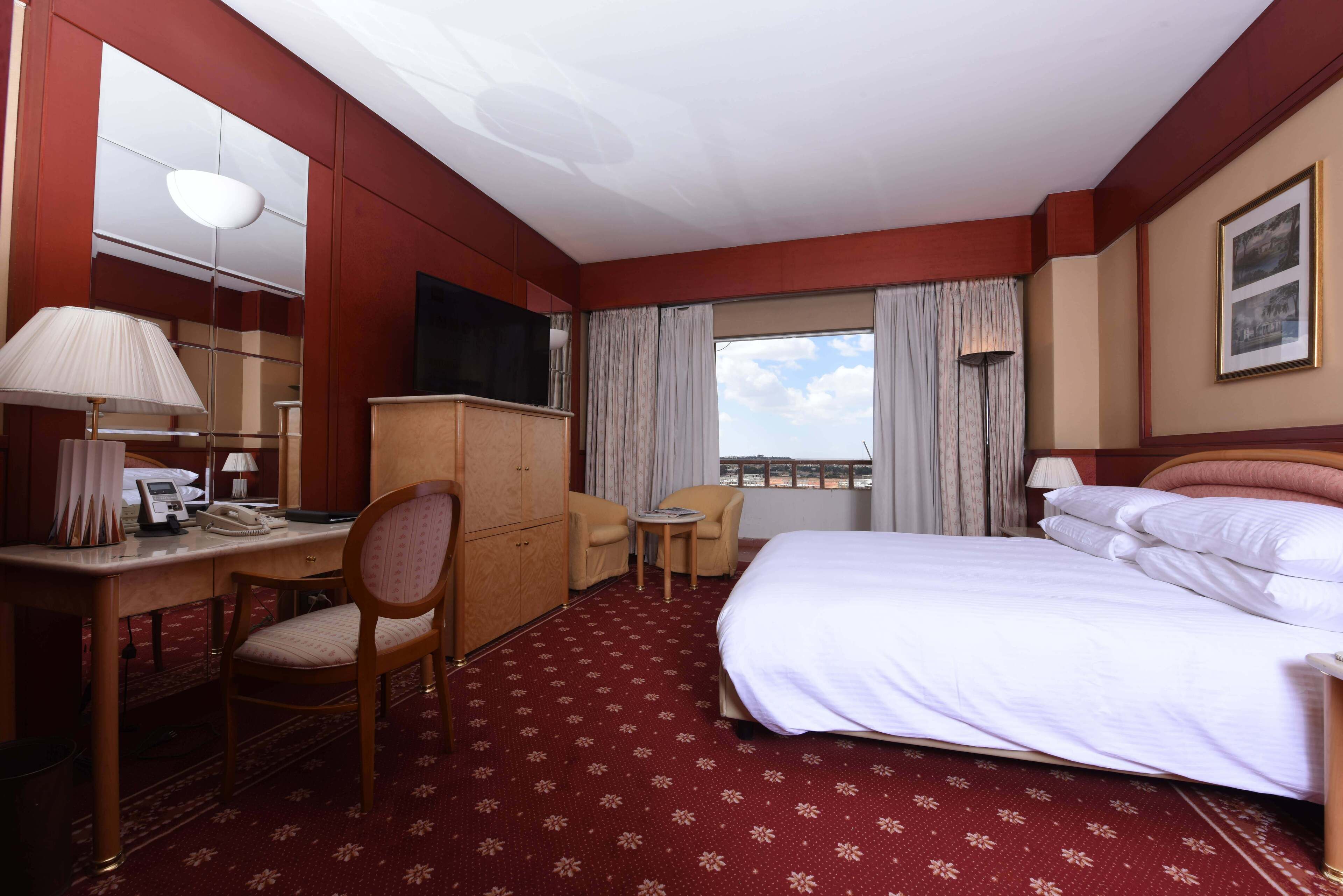 A hotel room with a bed, desk, chair, and a small table.