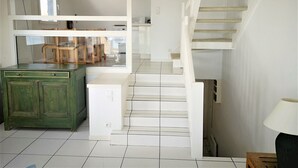 Interior moderno com escada, um armário verde e uma zona de refeições visível através de um painel de vidro.
