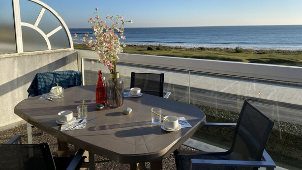 Uma mesa de jantar com cadeiras, um vaso de flores e vista para o oceano.