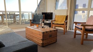 Uma sala de estar aconchegante com uma janela grande, um aparador de madeira, uma televisão e duas cadeiras.