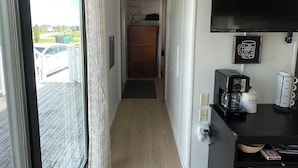 A narrow hallway with a sliding glass door leading to a balcony, a black coffee station, and a TV mounted on the wall.