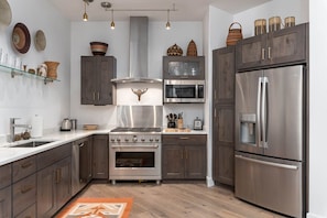 Une cuisine moderne avec des meubles en bois foncé, des appareils électroménagers en acier inoxydable et une étagère en verre où sont exposés des objets décoratifs.