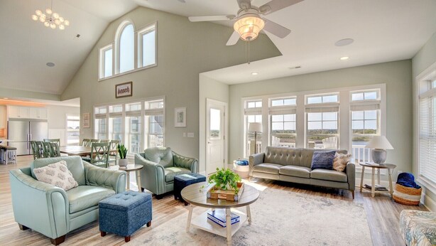 A spacious living room with a high ceiling, large windows, and a view of the outdoors. - Enjoy Sounds Beachy, an 8-bedroom haven in North Topsail Beach, NC with stunning water views. (North Topsail Beach)