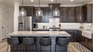 A modern kitchen with dark wood cabinets, a granite island with bar stools, stainless steel appliances, and pendant lighting. - Poolside on the 2nd Green - Game Room, Sleeps 12 (St. George)