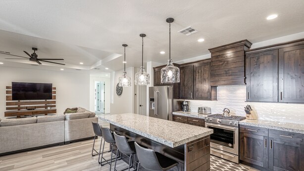 A modern kitchen with dark wood cabinets, granite countertops, and stainless steel appliances. There is a bar area with stools and a large island. - Poolside on the 2nd Green - Game Room, Sleeps 12 (St. George)