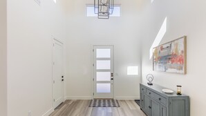A hallway with a light wooden floor, a gray cabinet with a mirror and a plate, and a door with frosted glass panels. - Poolside on the 2nd Green - Game Room, Sleeps 12 (St. George)