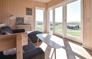 A modern room with a wooden interior, a sofa, a small table, and large windows offering a view of the outdoors. - Cozy home in Faaborg with sauna (Faaborg)