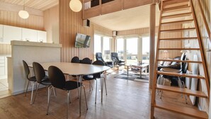 Une pièce spacieuse avec un plancher en bois, une grande table ronde entourée de chaises, un canapé, un téléviseur fixé au mur et un escalier en bois.