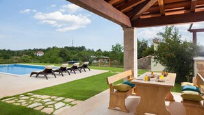 Eine Terrasse im Freien mit Pool, Liegestühlen und einem Holztisch mit Kissen.