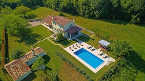 An aerial view of a house with a swimming pool, a patio with lounge chairs, and a garden area.