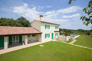 A two-story house with a tiled roof, green shutters, and a swimming pool in the backyard.