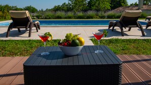Ein Poolbereich mit einem Tisch, auf dem sich eine Obstschale und zwei Martini-Gläser befinden.