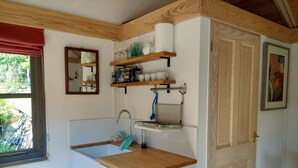 A compact kitchen with a sink, wooden countertop, and shelves above the sink.