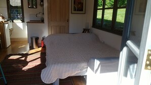 A bedroom with a bed, a window, a door, a radiator, a trash bin, and a rug.