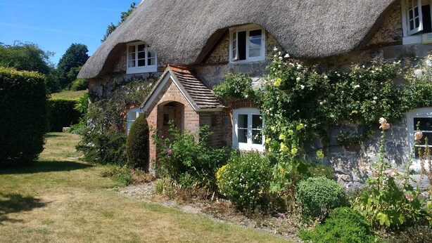 A traditional thatched-roof house with a brick archway and a small garden area.