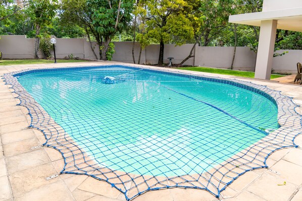 A swimming pool with a blue net surrounding it, set against a backdrop of trees and a building.