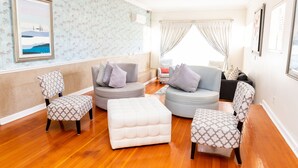 Een woonkamer met gestreept fauteuils, een gebonden poef en een grijze bank met kussens.