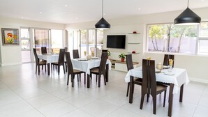 Een ruime eethoek met meerdere tafels en stoelen, een flatscreen-tv aan de muur en grote ramen voor natuurlijk licht.
