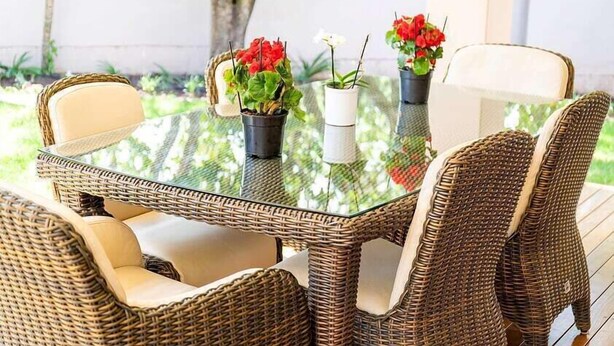 Een rieten eettafel met stoelen, omringd door potplanten.