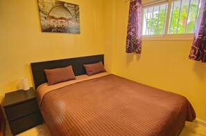 Une chambre à coucher avec un lit, une table de chevet, un tableau au mur et une fenêtre avec des rideaux.