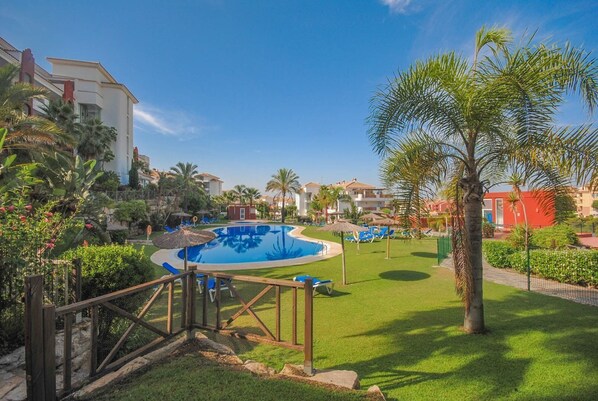 A pool area with a clear blue pool, surrounded by well-maintained grass, palm trees, and lounge chairs.