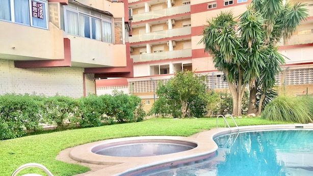 Piscina com hidromassagem, rodeada por um gramado bem cuidado e palmeiras.