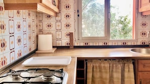 Uma cozinha com fogão a gás, janela com vista para árvores e azulejos estampados nas paredes.