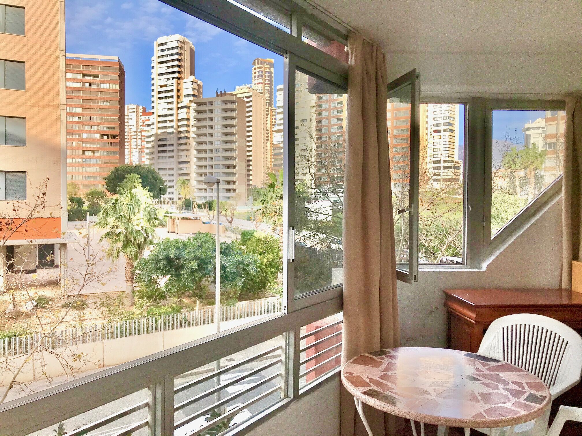 A balcony with a view of high-rise buildings, a table, and a chair.