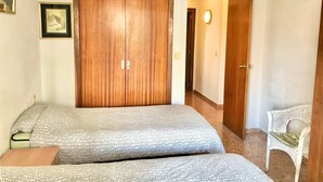 Quarto com duas camas, um guarda-roupa de madeira, um quadro na parede e uma cadeira branca.