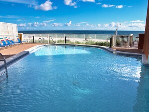 Piscina com vista para o oceano, área cercada com espreguiçadeiras e céu claro.