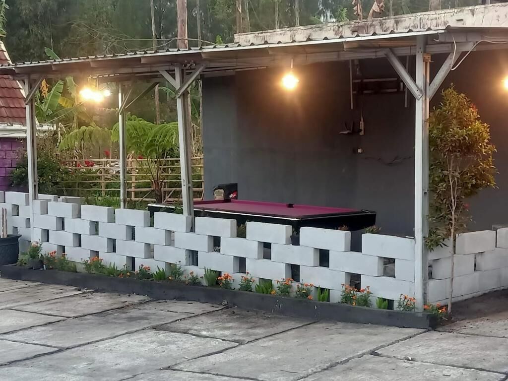 A covered outdoor area with a pool table, surrounded by a white brick wall and a concrete floor.