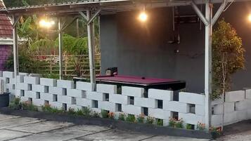 A covered outdoor area with a pool table, surrounded by a white brick wall and a concrete floor.
