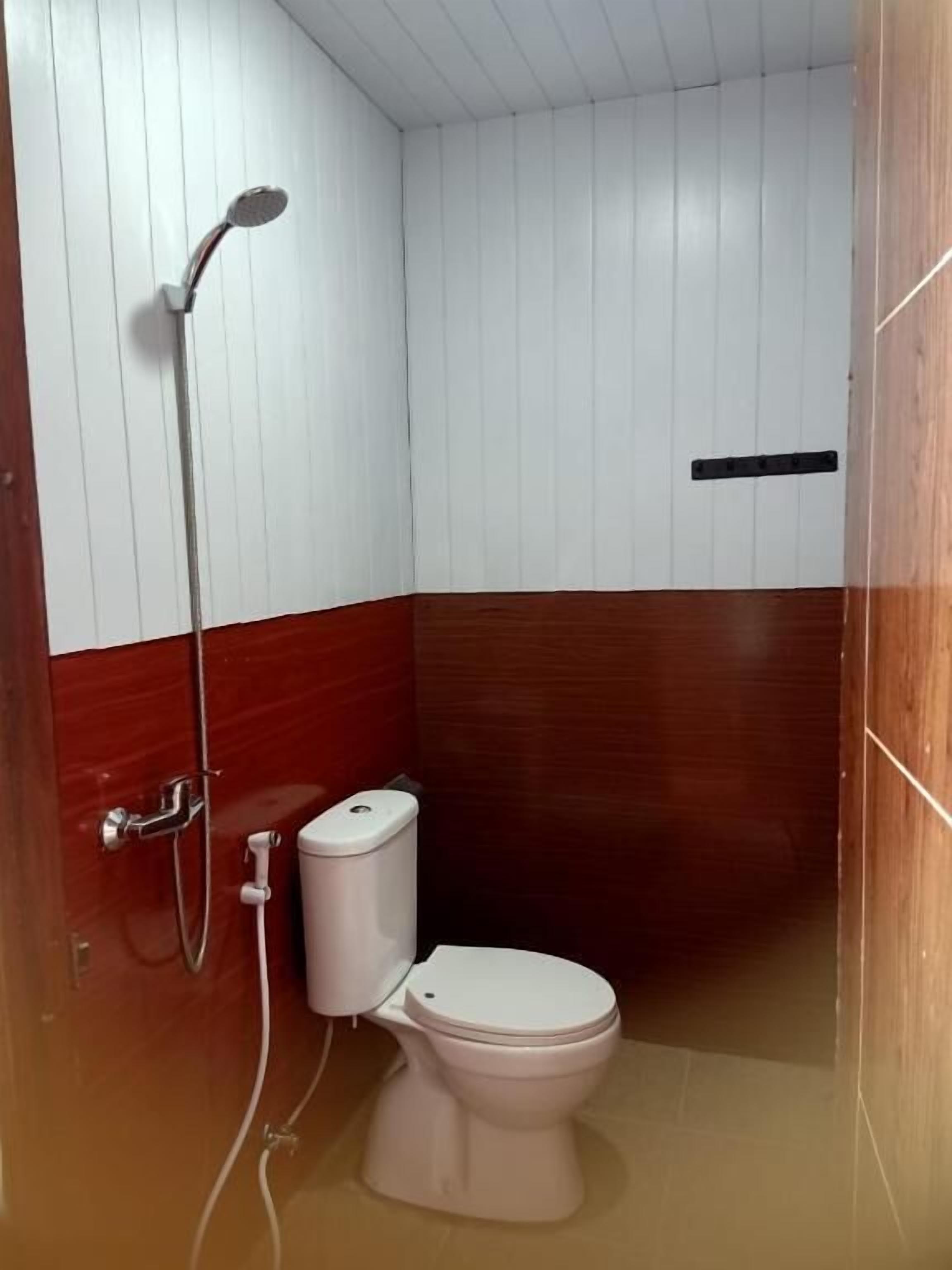 A small bathroom with a white toilet, a shower, and wooden paneling on the walls.
