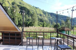Un bâtiment en bois doté d’un toit en pente, d’un balcon avec des rampes en métal et offrant une vue sur une colline boisée.