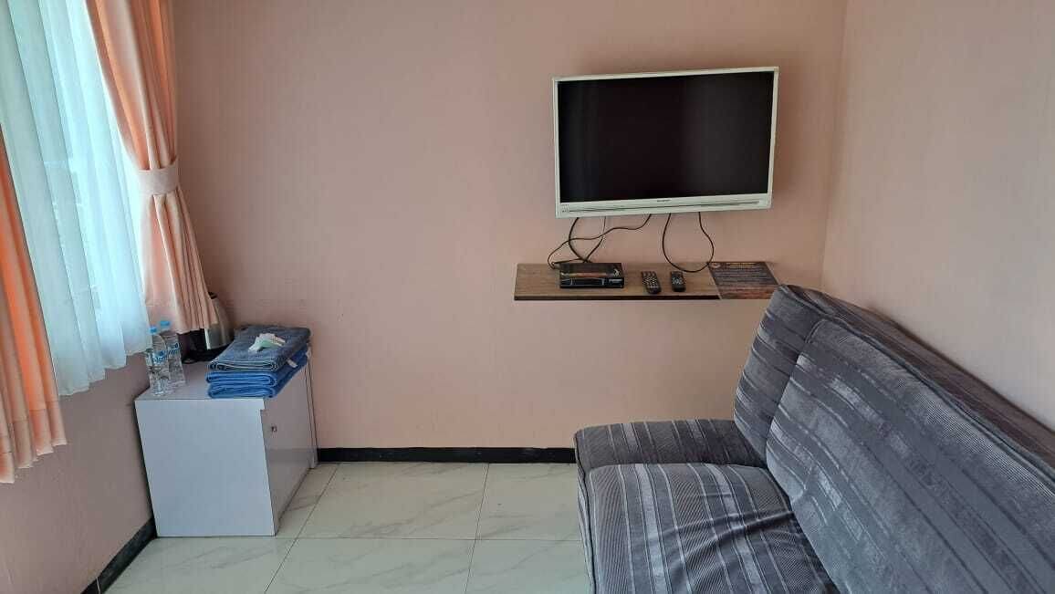 Una habitación con una televisión montada en la pared, un sofá, una mesita con un control remoto y un armario con ropa doblada.