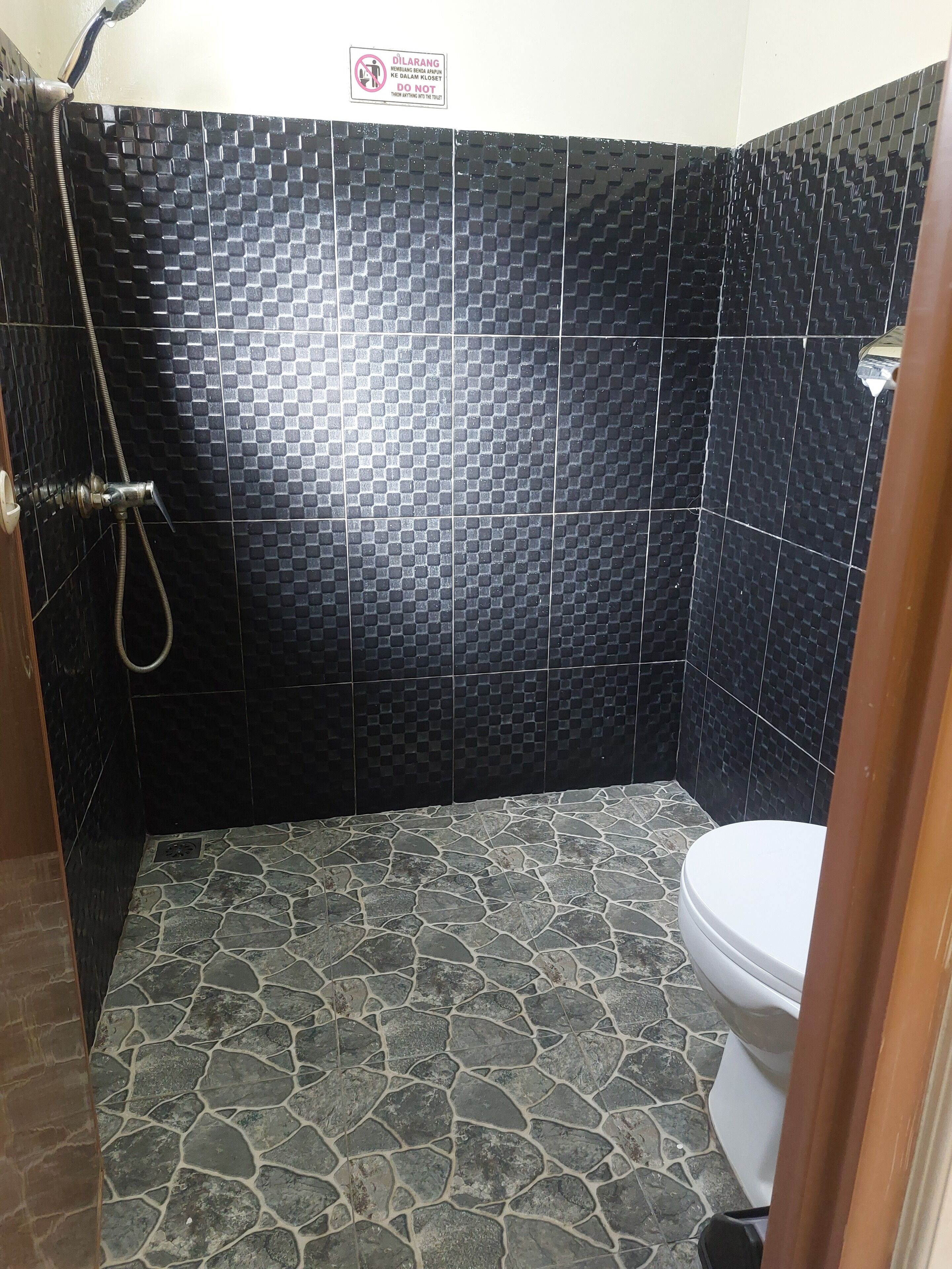 Un baño con paredes de azulejos negros, suelo de piedra y un inodoro blanco.
