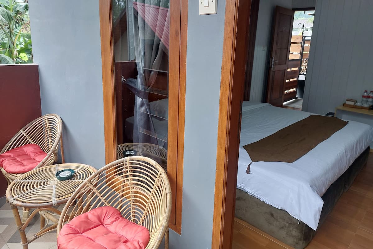 Ein Zimmer mit einem Bett, zwei Korbstühlen mit Kissen, einem kleinen Tisch und einem Fenster mit Vorhang.