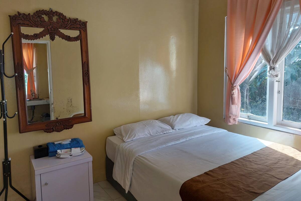 Ein Schlafzimmer mit einem Bett, einem Schminktisch, einem Spiegel und einem Fenster mit Vorhängen.